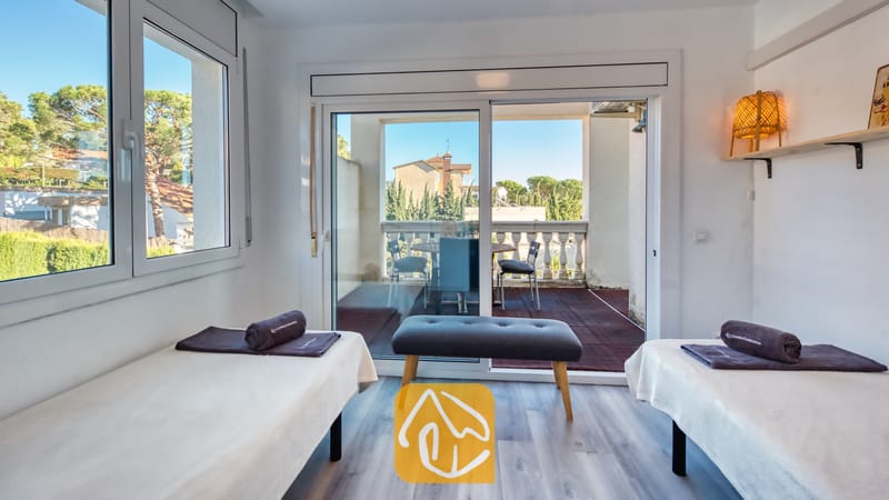 Villas de vacances Costa Brava Espagne - Villa Madonna - Chambre à lits jumeaux de la Villa Madonna comprenant deux lits simples, des serviettes roulées gris foncé, un banc en bois et des baies vitrées coulissantes s'ouvrant sur un balcon.