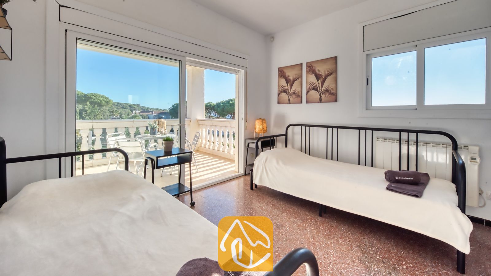 Vakantievilla's Costa Brava Spanje - Villa Madonna - Tweepersoonskamer met twee eenpersoonsbedden met een zwart metalen frame, wit beddengoed en een schuifpui die uitkomt op een zonnig balkon bij Villa Madonna.