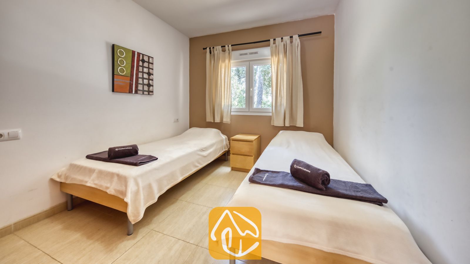 Vakantievilla's Costa Brava Spanje - Villa Esmee - Slaapkamer met twee eenpersoonsbedden voorzien van witte spreihoevens, donkere opgerolde handdoeken, een houten nachtkastje en een klein raam met beige gordijnen.