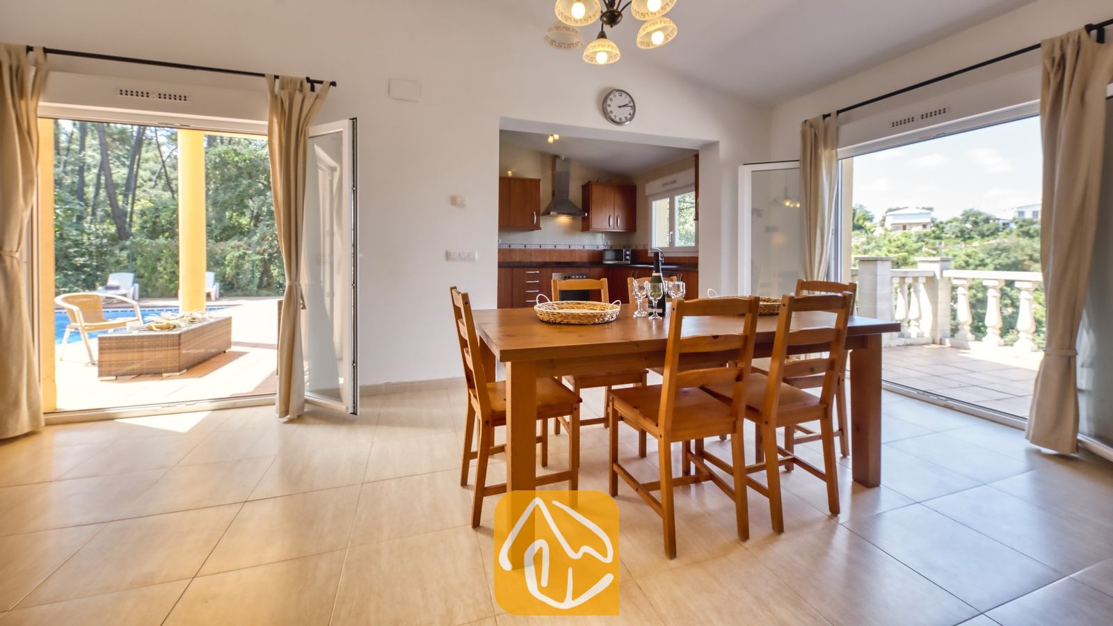 Vakantievilla's Costa Brava Spanje - Villa Esmee - Houten eettafel en stoelen in de open woonkamer van Villa Esmee, geflankeerd door openslaande glazen deuren die uitzicht bieden op de buitenterrassen.