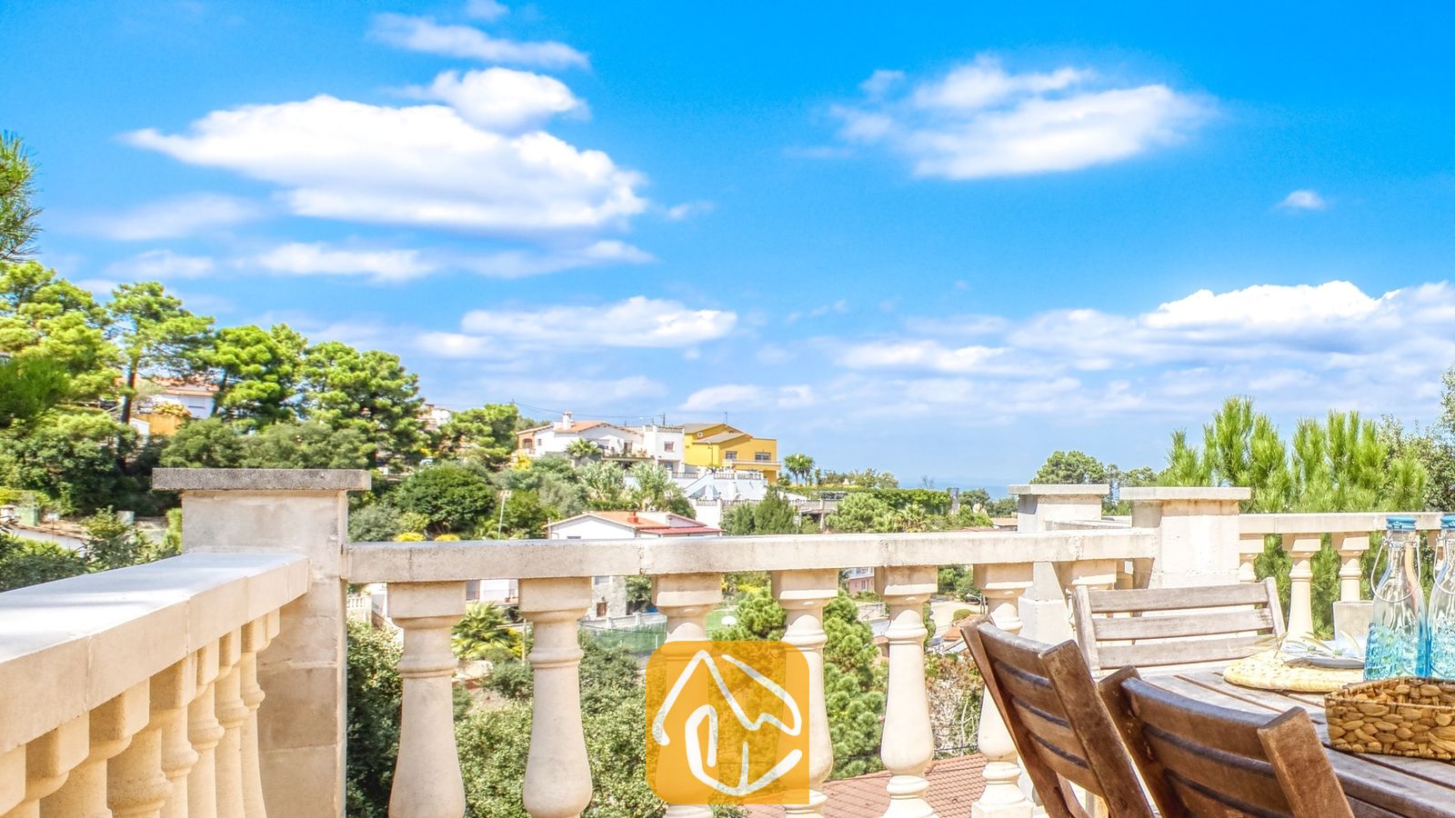 Vakantievilla's Costa Brava Spanje - Villa Esmee - Balkonterras bij Villa Esmee met uitzicht op groene heuvels en in de verte gelegen huizen onder een blauwe lucht met witte wolken.