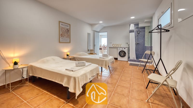 Holiday villas Costa Brava Spain - Villa La Luna - Guest bedroom with two twin beds, terracotta tile flooring, bedside lamps, and an ensuite shower area with blue mosaic tiles.