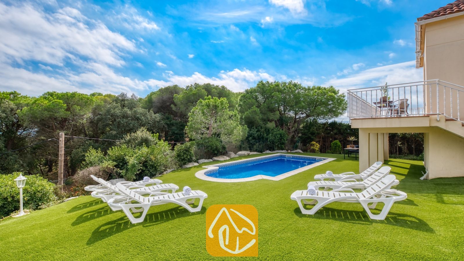 Vakantievilla's Costa Brava Spanje - Villa La Luna - Buitenzwembad omringd door een groene grasmat en witte ligstoelen bij Villa La Luna in Spanje, tegen een achtergrond van bomen en een blauwe lucht.