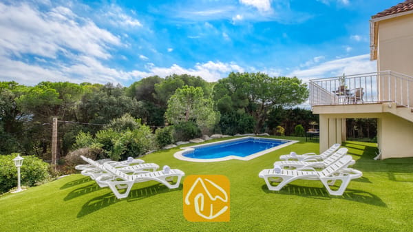Vakantievilla's Costa Brava Spanje - Villa La Luna - Buitenzwembad omringd door een groene grasmat en witte ligstoelen bij Villa La Luna in Spanje, tegen een achtergrond van bomen en een blauwe lucht.