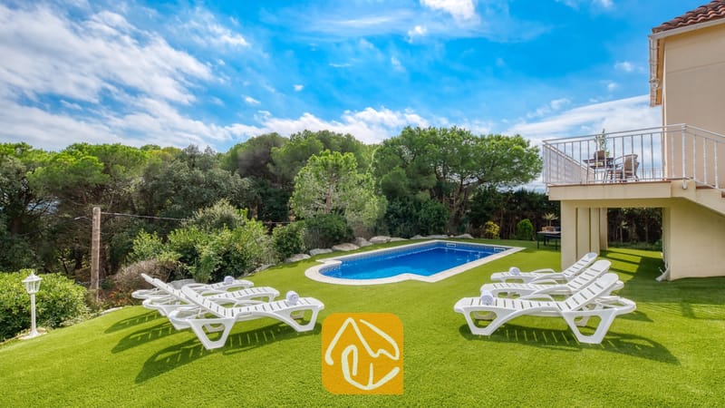 Vakantievilla's Costa Brava Spanje - Villa La Luna - Buitenzwembad omringd door een groene grasmat en witte ligstoelen bij Villa La Luna in Spanje, tegen een achtergrond van bomen en een blauwe lucht.