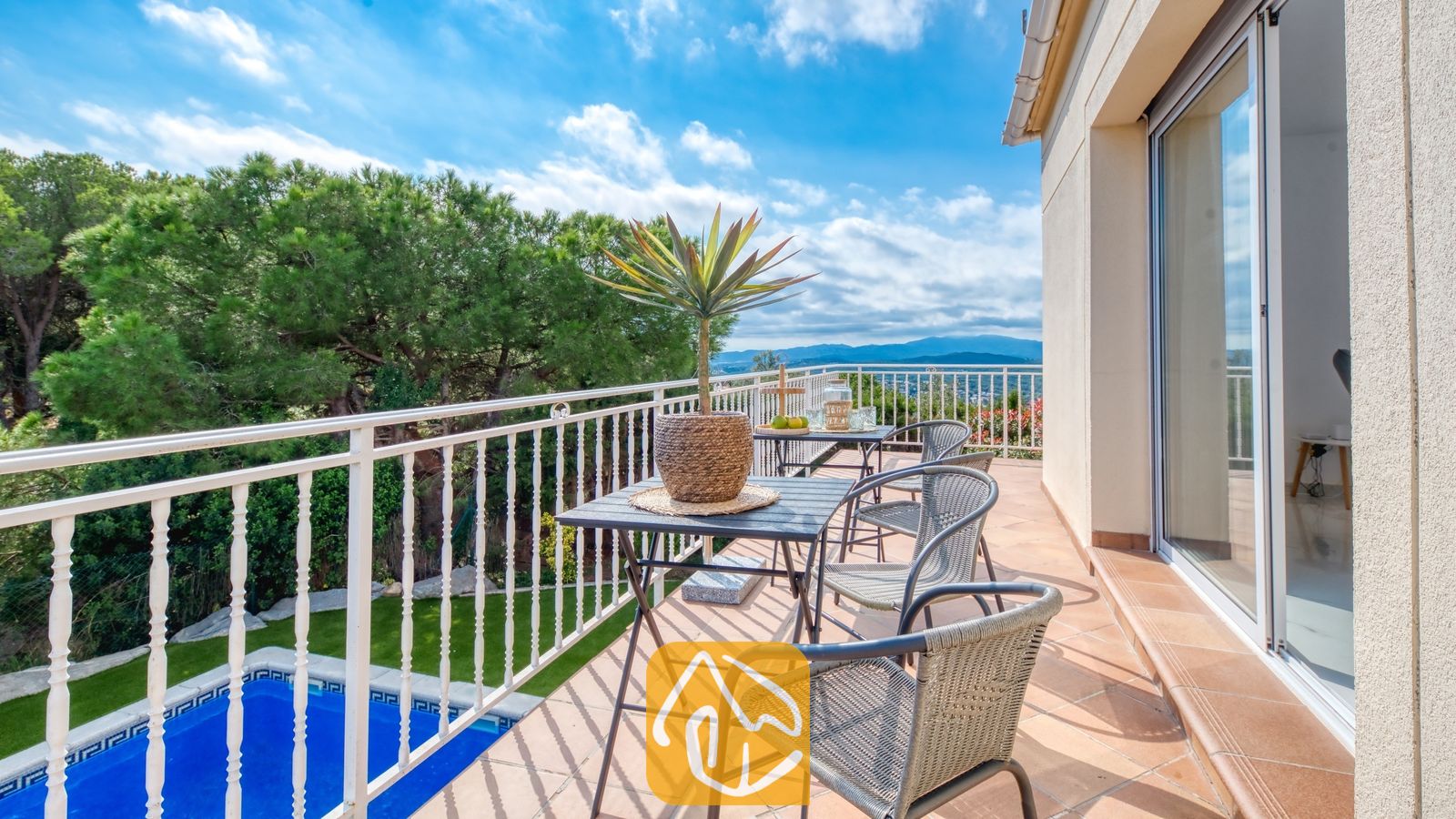 Vakantievilla's Costa Brava Spanje - Villa La Luna - Terras van Villa La Luna met een buitenetablissement, een potplant en een witte reling met uitzicht op een zwembad en bomen.