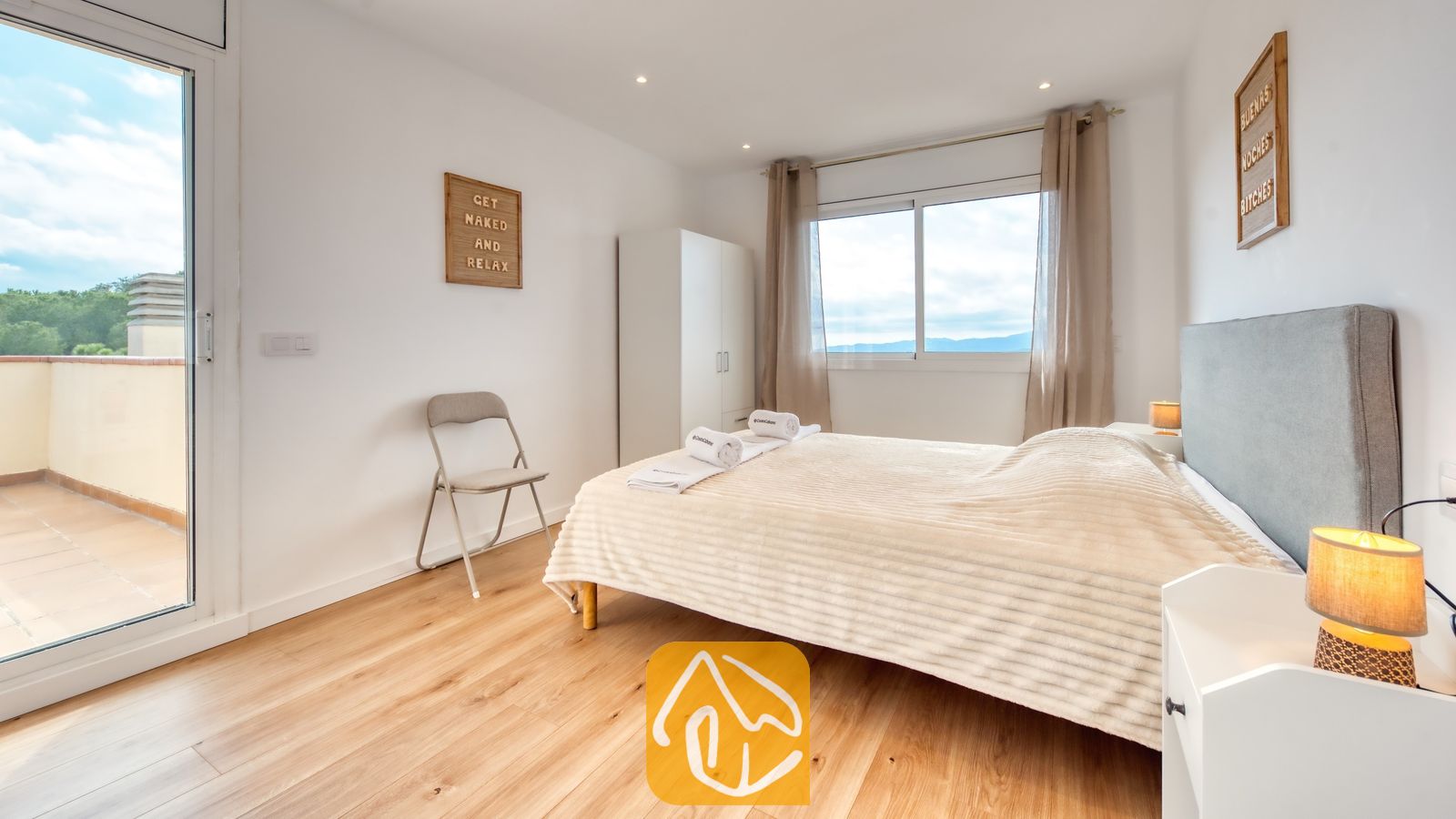 Vakantievilla's Costa Brava Spanje - Villa La Luna - Slaapkamer met een tweepersoonsbed, lichte houten vloer, nachtkastlampje en een glazen schuifdeur naar een buitenterras.