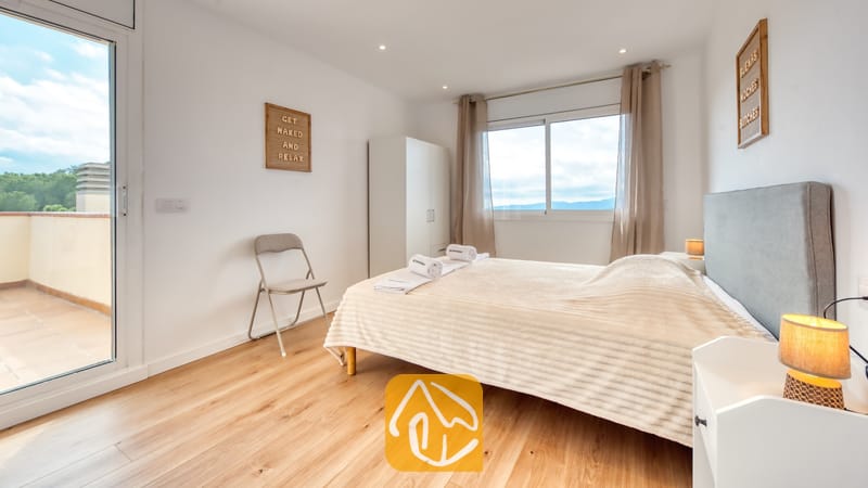 Holiday villas Costa Brava Spain - Villa La Luna - Bedroom with a double bed, light wood flooring, bedside lamp, and sliding glass door leading to an outdoor terrace.