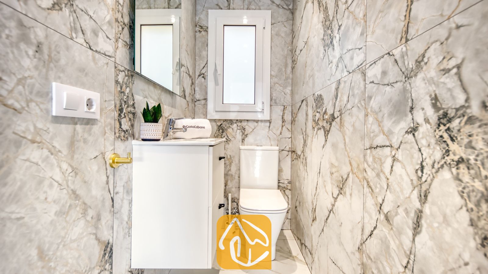 Vakantievilla's Costa Brava Spanje - Villa La Luna - Modern badkamerinterieur met grijs gemarmerde tegelwanden, een wit badkamermeubel met wastafel, een toilet en een klein raam daarboven.