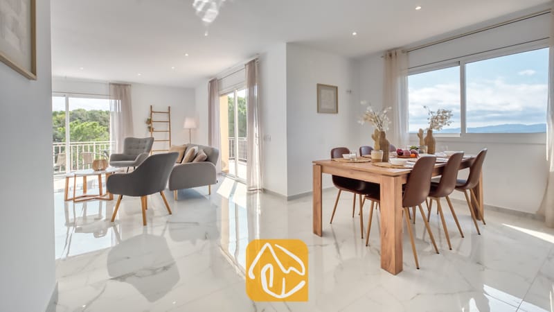 Vakantievilla's Costa Brava Spanje - Villa La Luna - Open woon- en eetgedeelte in Villa La Luna met wit marmeren vloeren, een houten eettafel met bruine stoelen en een grijze bank.