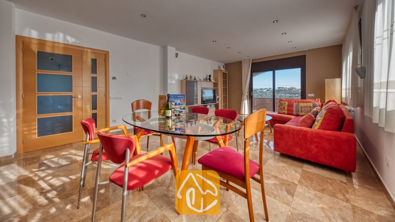 Vakantievilla's Costa Brava Spanje - Villa Grace - Ruime woon- en eetkamer in Villa Grace, voorzien van een glazen eettafel met rode stoelen en een aangrenzende rode hoekbank.