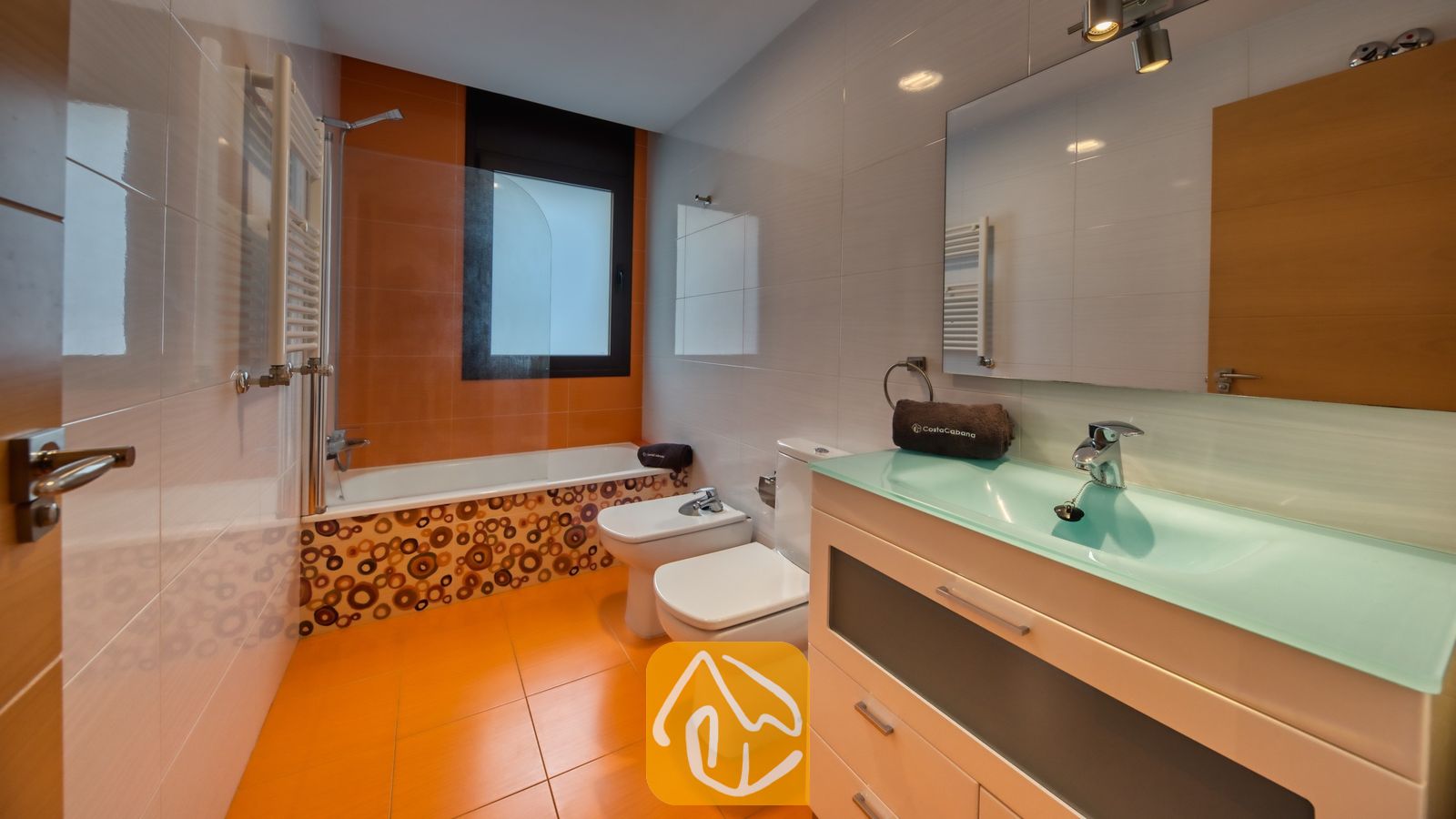 Vakantievilla's Costa Brava Spanje - Villa Grace - Moderne badkamer met oranje tegelvloer, een wastafelmeubel met glazen blad en een ligbad met een decoratief mozaïek voorpaneel.