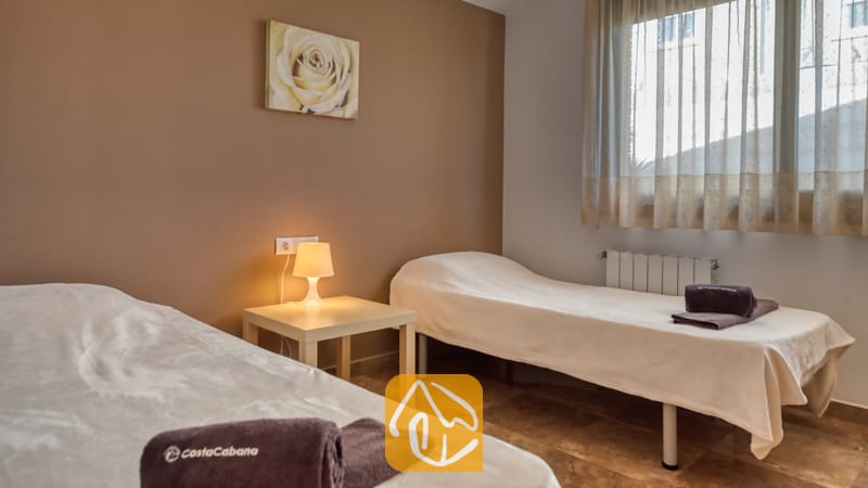 Villas de vacances Costa Brava Espagne - Villa Grace - Chambre à lits jumeaux avec deux lits simples habillés de linge blanc, une table de chevet partagée avec une petite lampe et une décoration murale marron à la Villa Grace.