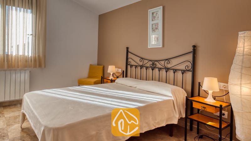 Villas de vacances Costa Brava Espagne - Villa Grace - Chambre avec un lit en fer forgé noir, du linge de lit blanc, deux petites tables de chevet avec lampes, et un fauteuil jaune dans le coin
