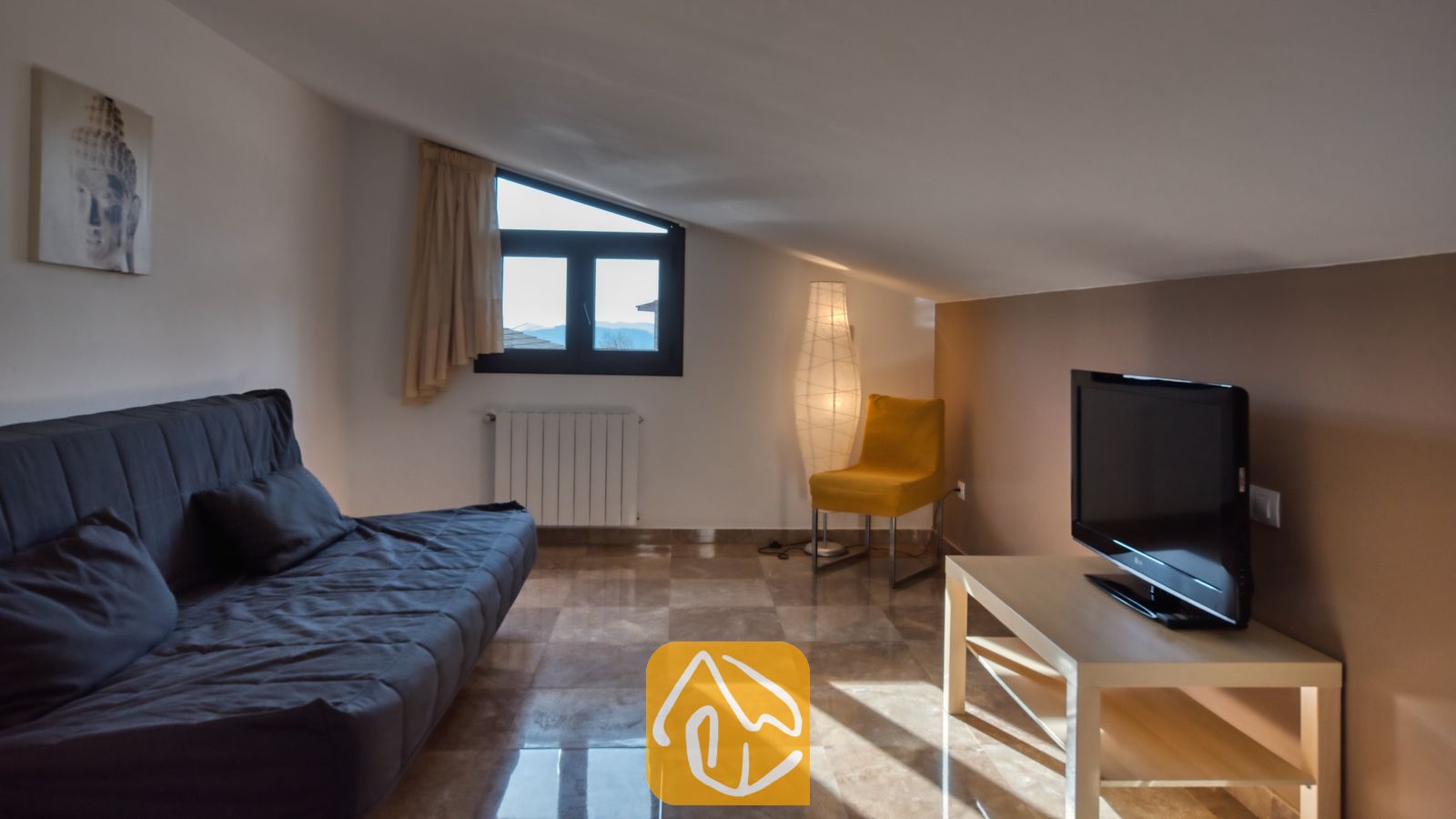 Vakantievilla's Costa Brava Spanje - Villa Grace - Woonkamer op de zolderverdieping met een schuin dak, voorzien van een donkergrijze bank, een gele fauteuil, een televisie op een licht houten meubel en een tegelvloer.