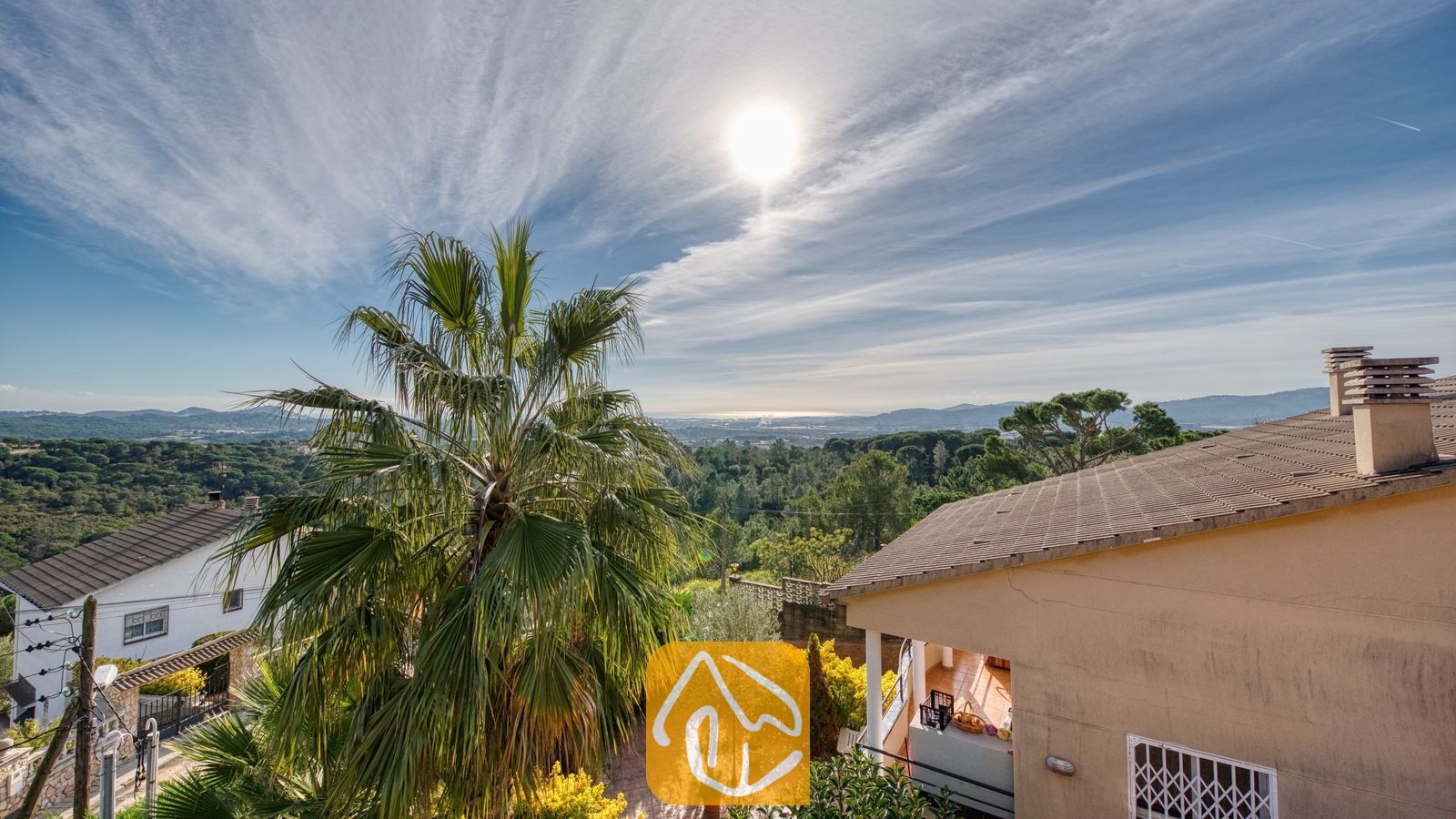 Vakantievilla's Costa Brava Spanje - Villa Grace - Zonnig uitzicht over een groen landschap met een palmboom en dakpannen bij Villa Grace in Spanje