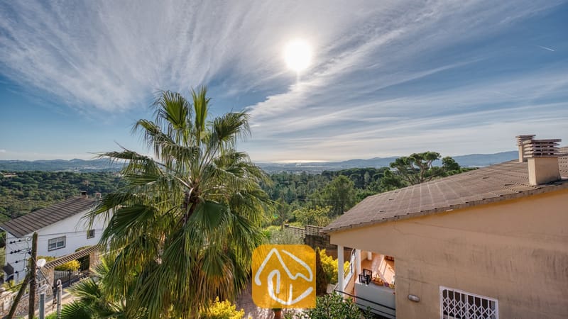 Villas de vacances Costa Brava Espagne - Villa Grace - Vue ensoleillée sur un paysage verdoyant avec un palmier et des toits de tuiles près de la Villa Grace en Espagne