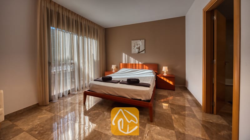 Villas de vacances Costa Brava Espagne - Villa Grace - Chambre à coucher avec un cadre de lit en bois, des rideaux vaporeux du sol au plafond et un sol carrelé à la Villa Grace