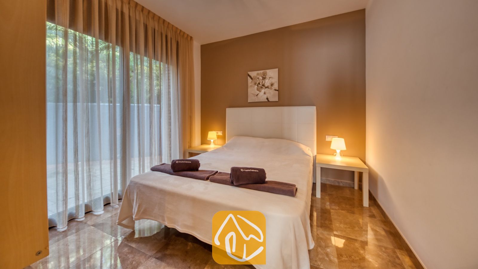 Vakantievilla's Costa Brava Spanje - Villa Grace - Slaapkamer met een tweepersoonsbed, witte nachtkastjes met verlichte schemerlampen en inbetween gordijnen voor de glazen schuifpui in Villa Grace.