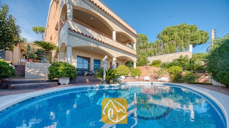 Vakantievilla's Costa Brava Spanje - Villa Grace - Gebogen zwembad met een mozaïektegelvloer, gelegen voor de meeverdiepingsbuitenkant van Villa Grace, voorzien van stenen bogen en balkons onder een helderblauwe hemel.