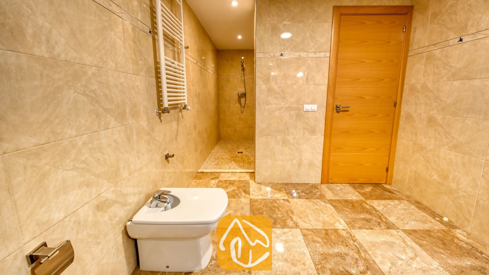 Vakantievilla's Costa Brava Spanje - Villa Grace - Betegelde badkamer met muren van beige marmer, een wit bidet, een inloopdouche en een houten binnendeur.