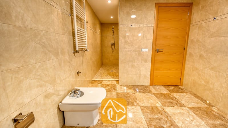 Vakantievilla's Costa Brava Spanje - Villa Grace - Betegelde badkamer met muren van beige marmer, een wit bidet, een inloopdouche en een houten binnendeur.