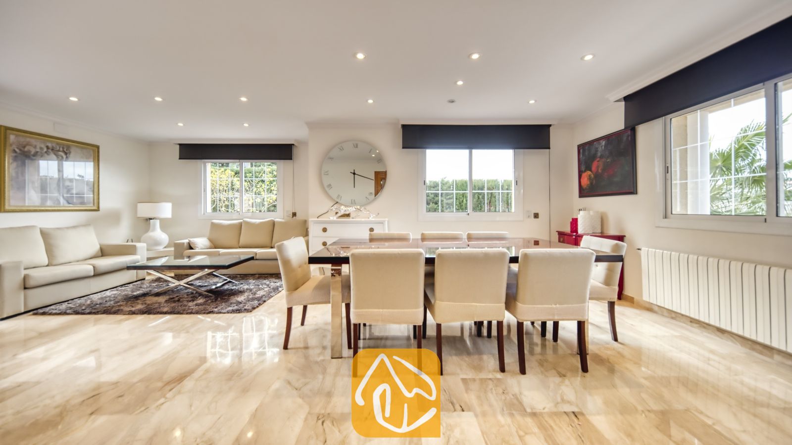 Vakantievilla's Costa Brava Spanje - Villa Lorena - Ruime, open woon- en eetkamer in Villa Lorena, voorzien van gepolijste marmeren vloeren, een donkerhouten eettafel met crèmekleurige stoelen en een zithoek met beige banken.