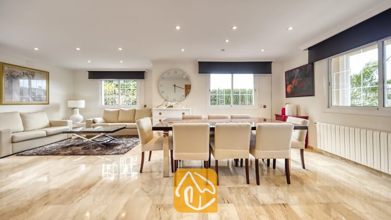 Vakantievilla's Costa Brava Spanje - Villa Lorena - Ruime, open woon- en eetkamer in Villa Lorena, voorzien van gepolijste marmeren vloeren, een donkerhouten eettafel met crèmekleurige stoelen en een zithoek met beige banken.