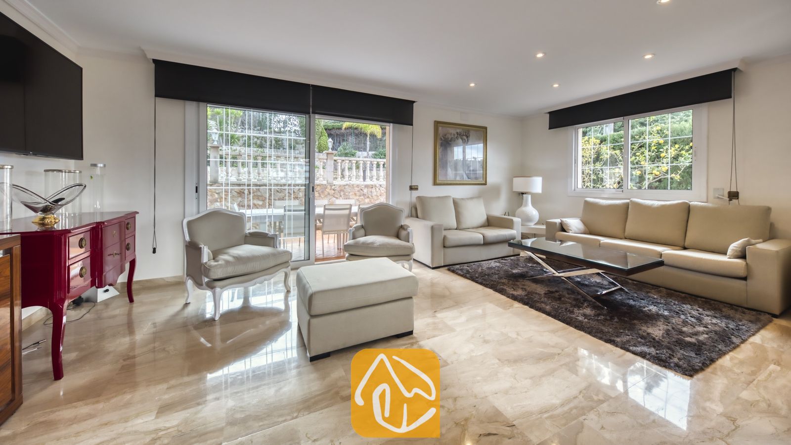 Vakantievilla's Costa Brava Spanje - Villa Lorena - Ruime woonkamer in Villa Lorena, voorzien van beige leren banken, een glazen salontafel op een donker vloerkleed en glazen schuifdeuren die toegang bieden tot een terras.