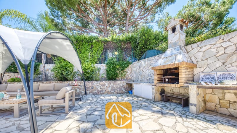 Vakantievilla's Costa Brava Spanje - Villa Lorena - Buitenbarbecuezone bij Villa Lorena, voorzien van een stenen grill, een terras met zitgedeelte onder een witte luifel en een bestrating van natuursteen.