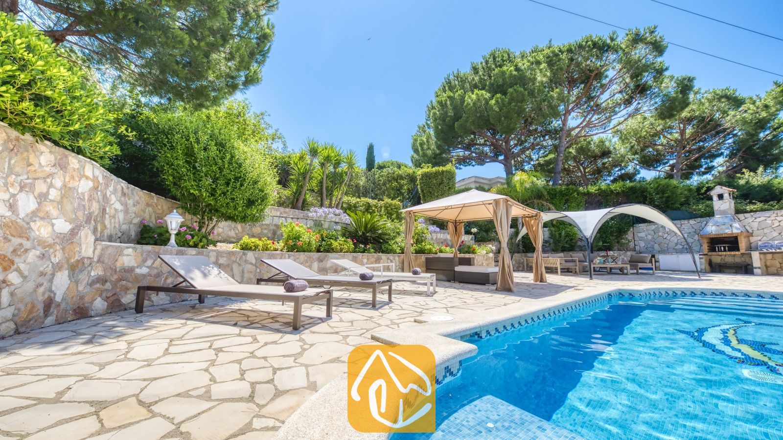 Vakantievilla's Costa Brava Spanje - Villa Lorena - Privézwembad met ligstoelen en een stenen terras bij Villa Lorena, omringd door dennenbomen, terrastuinen en een schaduwrijk prieel.