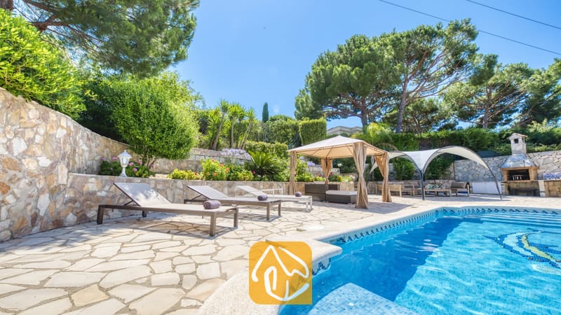 Vakantievilla's Costa Brava Spanje - Villa Lorena - Privézwembad met ligstoelen en een stenen terras bij Villa Lorena, omringd door dennenbomen, terrastuinen en een schaduwrijk prieel.