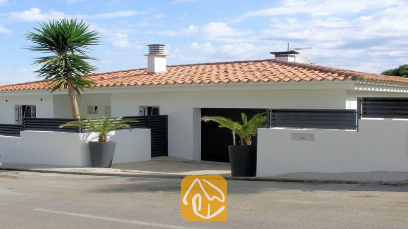 Villas de vacances Costa Brava Espagne - Villa Fransisca - Vue extérieure de la Villa Fransisca mettant en valeur ses murs blancs, son toit en tuiles orange, sa porte de garage sombre et ses palmiers en pot.