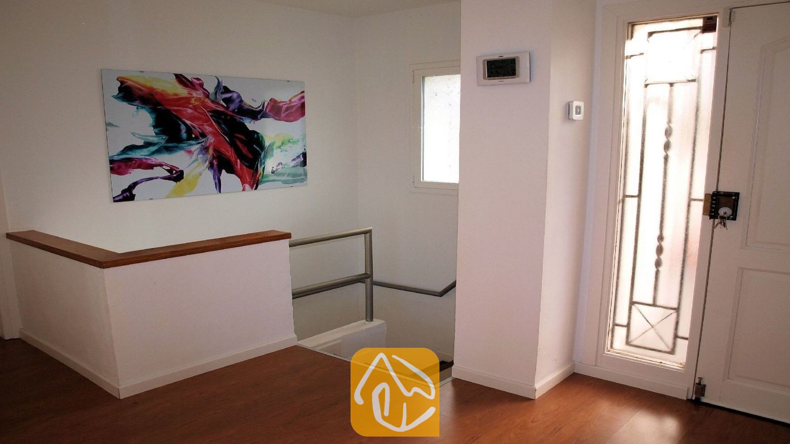 Vakantievilla's Costa Brava Spanje - Villa Fransisca - Overloop van de binnentrap met houten vloer, witte muren en een kleurrijk abstract schilderij op doek.