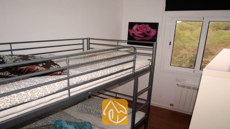 Villas de vacances Costa Brava Espagne - Villa Fransisca - Chambre avec lits superposés en métal gris, literie à motifs, œuvre murale représentant une rose rose et fenêtre offrant une vue sur les arbres.