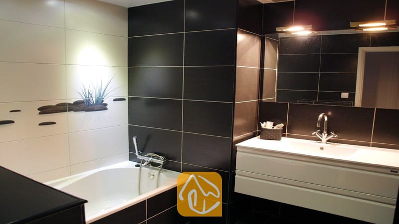 Villas de vacances Costa Brava Espagne - Villa Fransisca - Salle de bains moderne comprenant une baignoire blanche adjacente à un mur orné de carreaux noirs et blancs, un grand miroir et un meuble sous-vasque suspendu de couleur blanche.