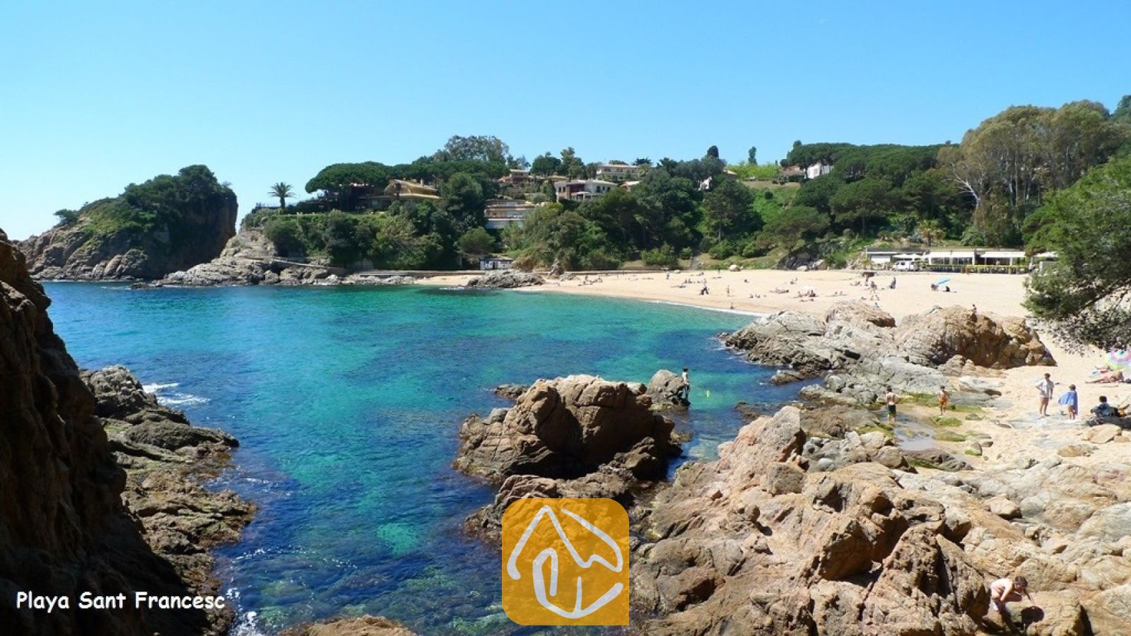 Vakantievilla's Costa Brava Spanje - Villa Fransisca - Een zandstrand bij Playa Sant Francesc, omlijst door rotsachtige kliffen en een turquoise zee onder een helderblauwe hemel.