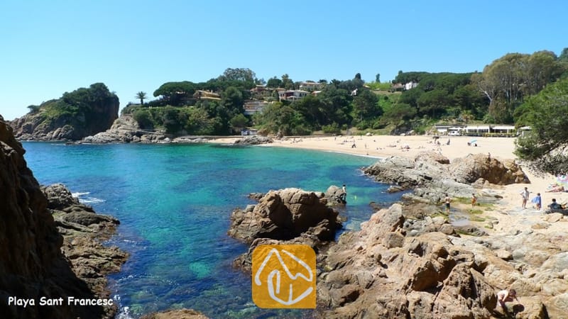 Villas de vacances Costa Brava Espagne - Villa Fransisca - Plage de sable fin à Playa Sant Francesc, encadrée par des falaises rocheuses et des eaux turquoise sous un ciel d'un bleu éclatant.