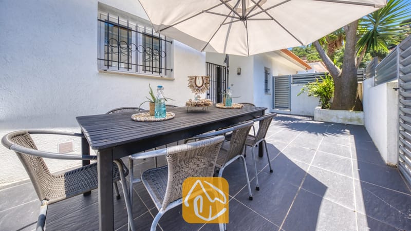 Vakantievilla's Costa Brava Spanje - Villa Fransisca - Buiten-eethoek bij Villa Fransisca met een donkerhouten tafel, omringd door geweven grijskleurige stoelen onder een grote witte parasol op een terras met tegels.