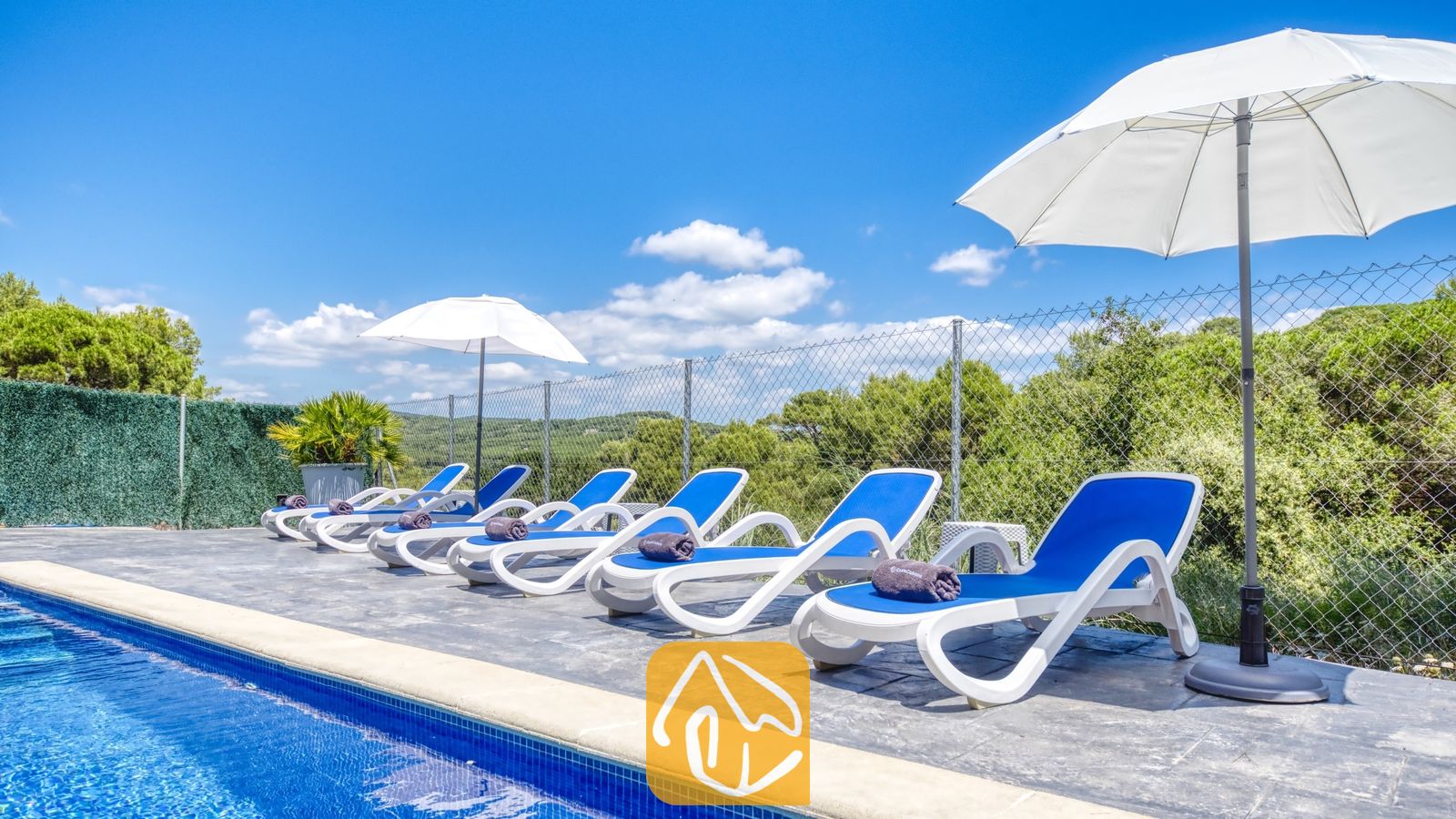 Vakantievilla's Costa Brava Spanje - Villa Fransisca - Witte en blauwe ligbedden staan opgesteld langs het zwembad van Villa Fransisca, vergezeld door witte parasols tegen een blauwe hemel.