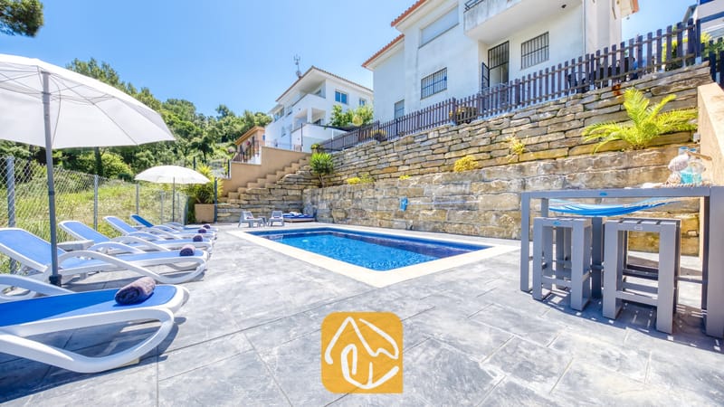 Vakantievilla's Costa Brava Spanje - Villa Fransisca - Privézwembad bij Villa Fransisca, voorzien van blauwe ligstoelen, witte parasols en een stenen keermuur onder een helderblauwe hemel