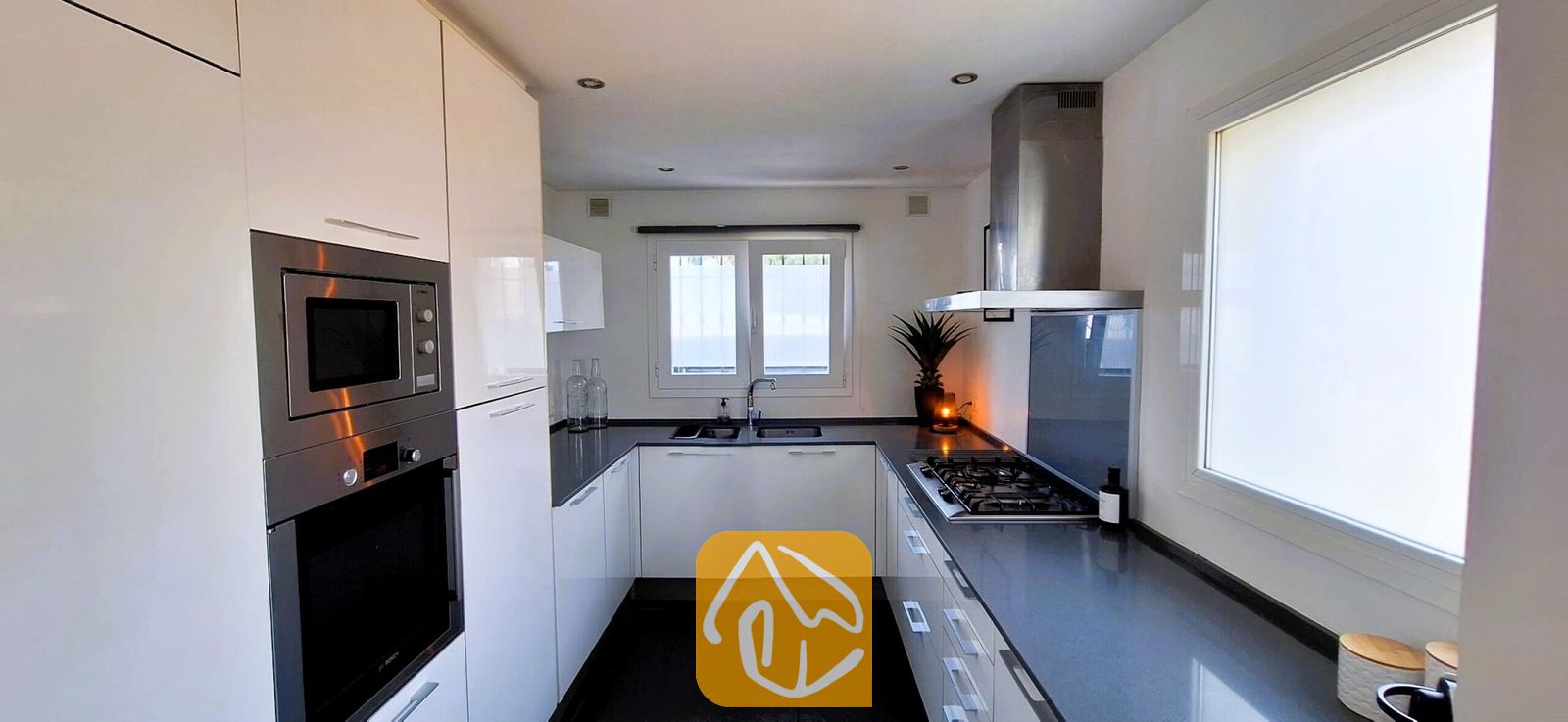 Vakantievilla's Costa Brava Spanje - Villa Fransisca - Moderne U-vormige keuken met witte kasten, donkere werkbladen, een ingebouwde rvs-oven en een gaskookplaat.
