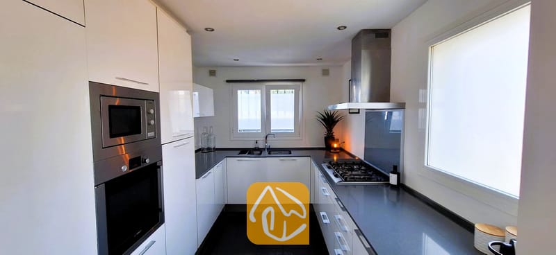 Villas de vacances Costa Brava Espagne - Villa Fransisca - Cuisine moderne en U dotée de placards blancs, de plans de travail sombres, d'un four encastré en acier inoxydable et d'une table de cuisson à gaz.