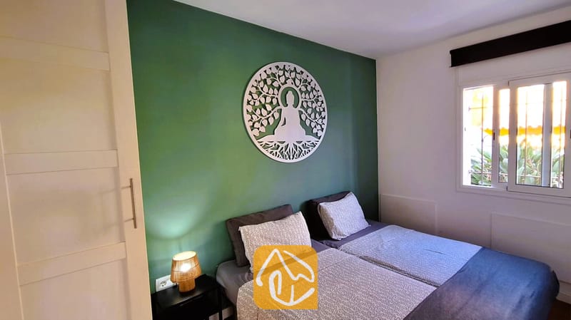 Villas de vacances Costa Brava Espagne - Villa Fransisca - Chambre avec deux lits simples adossés à un mur vert agrémenté d'une grande sculpture murale circulaire blanche et d'une lampe de chevet.