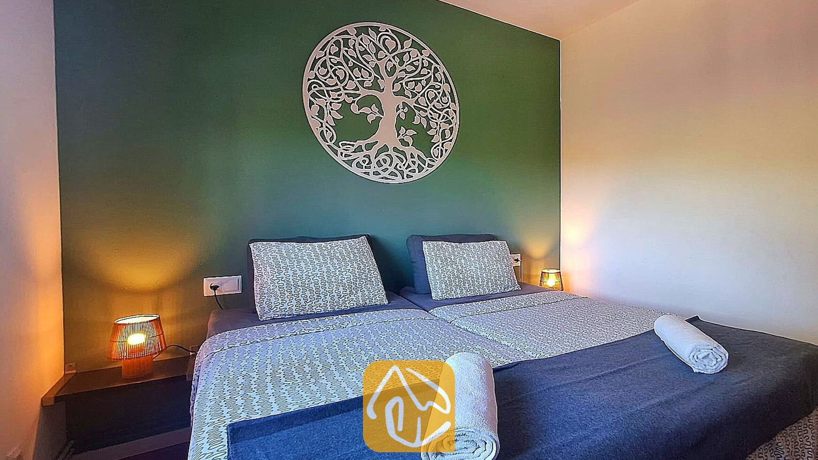 Vakantievilla's Costa Brava Spanje - Villa Fransisca - Slaapkamer met een tweepersoonsbed, een groene accentmuur met een wit levensboom-wandkleed en twee nachtkastlampjes.