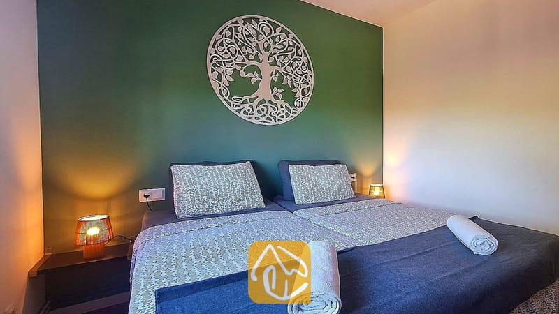 Villas de vacances Costa Brava Espagne - Villa Fransisca - Chambre avec un lit double, un mur d'accent vert doté d'une tenture murale blanche représentant un arbre de vie, et deux lampes de chevet.