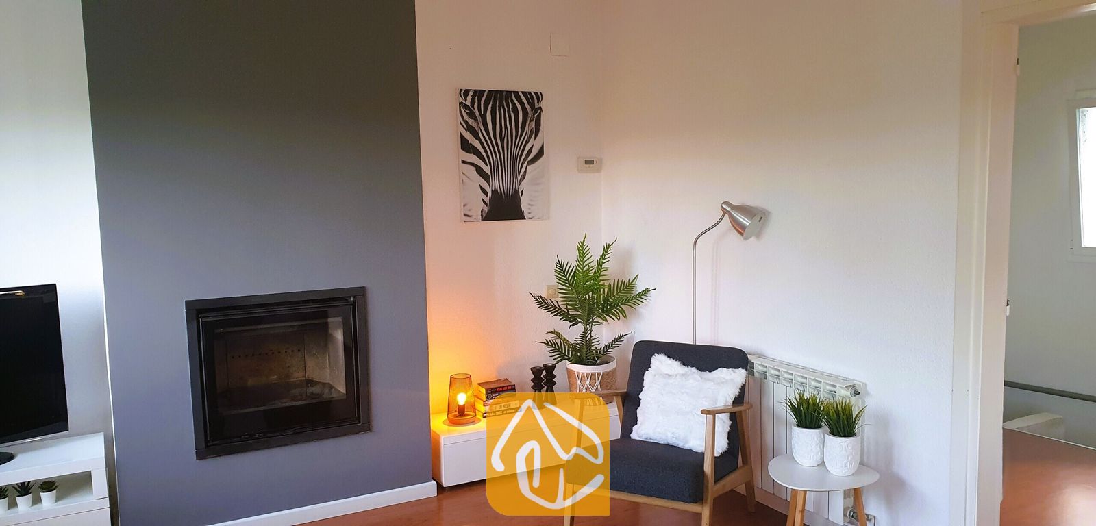 Vakantievilla's Costa Brava Spanje - Villa Fransisca - Zithoek met een donkergrijze fauteuil, een ingebouwde open haard tegen een grijze accentmuur en een wanddecoratie met zebraprint.