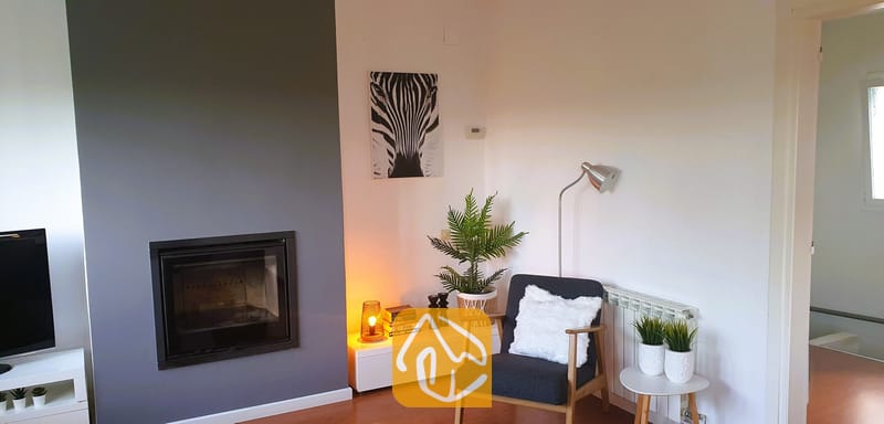 Villas de vacances Costa Brava Espagne - Villa Fransisca - Coin salon agrémenté d'un fauteuil gris foncé, d'une cheminée encastrée sur un mur d'accent gris et d'une impression murale motif zèbre.