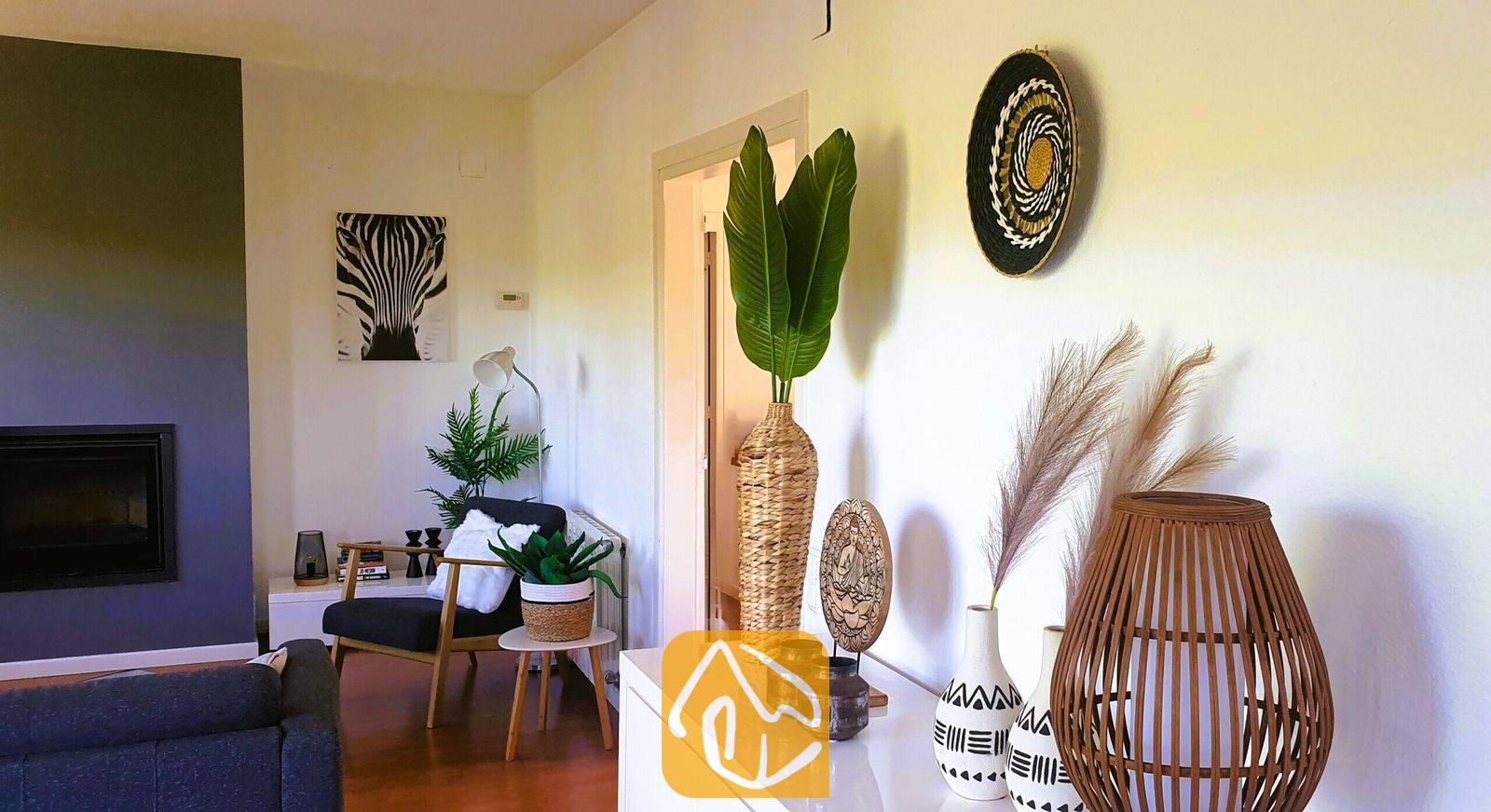 Vakantievilla's Costa Brava Spanje - Villa Fransisca - Interieur van de woonkamer met een wit dressoir voorzien van geweven vazen en pampasgras, een zwarte fauteuil en wanddecoratie met een zebra-motief.