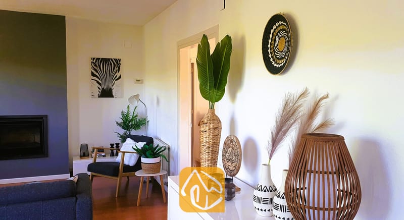 Villas de vacances Costa Brava Espagne - Villa Fransisca - Intérieur du salon comprenant un buffet blanc agrémenté de vases tressés et d'herbe de la pampa, un fauteuil noir et une œuvre murale représentant un zèbre.